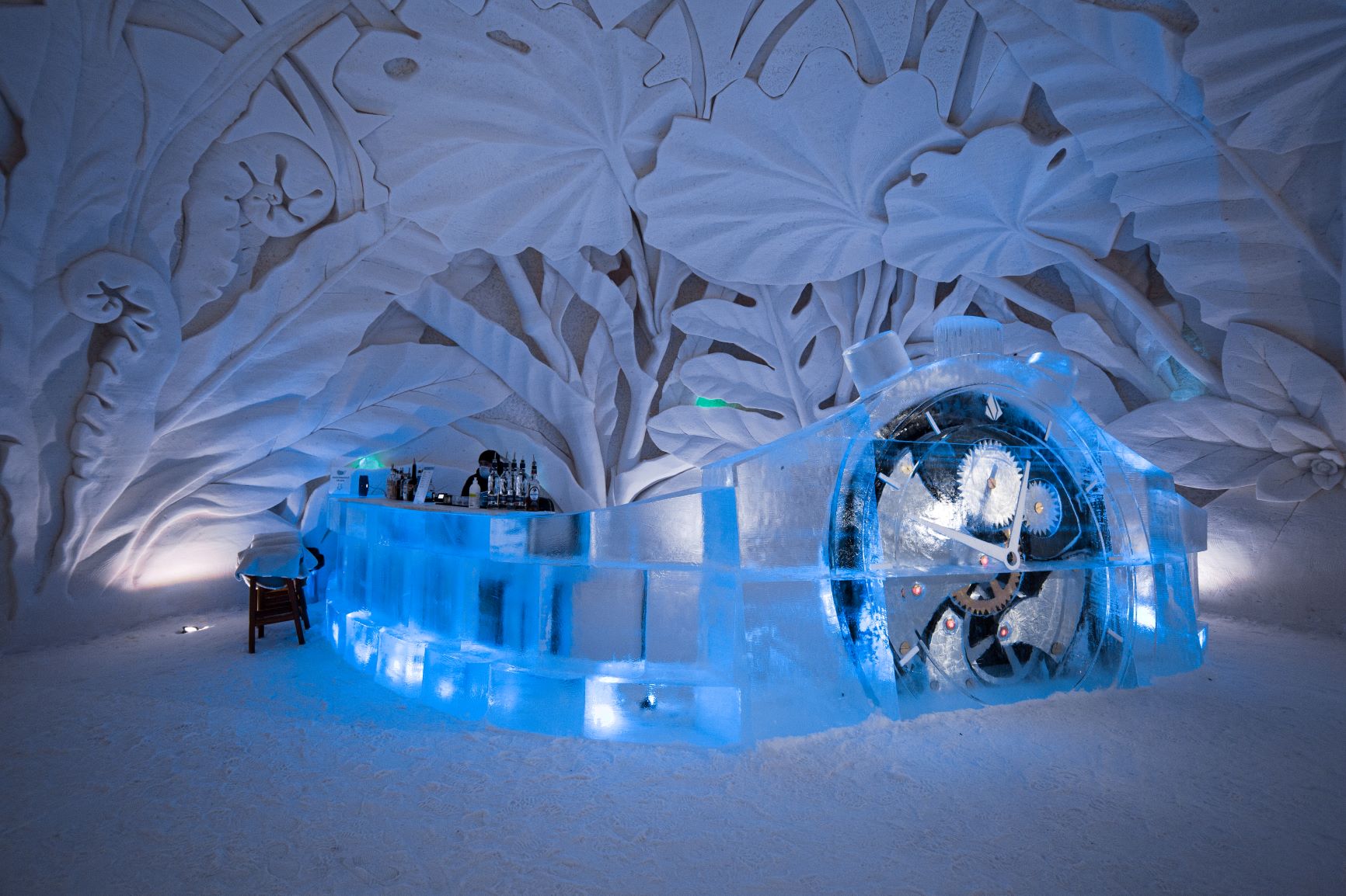Carved snow hall with columns and benches lit in pale blue light